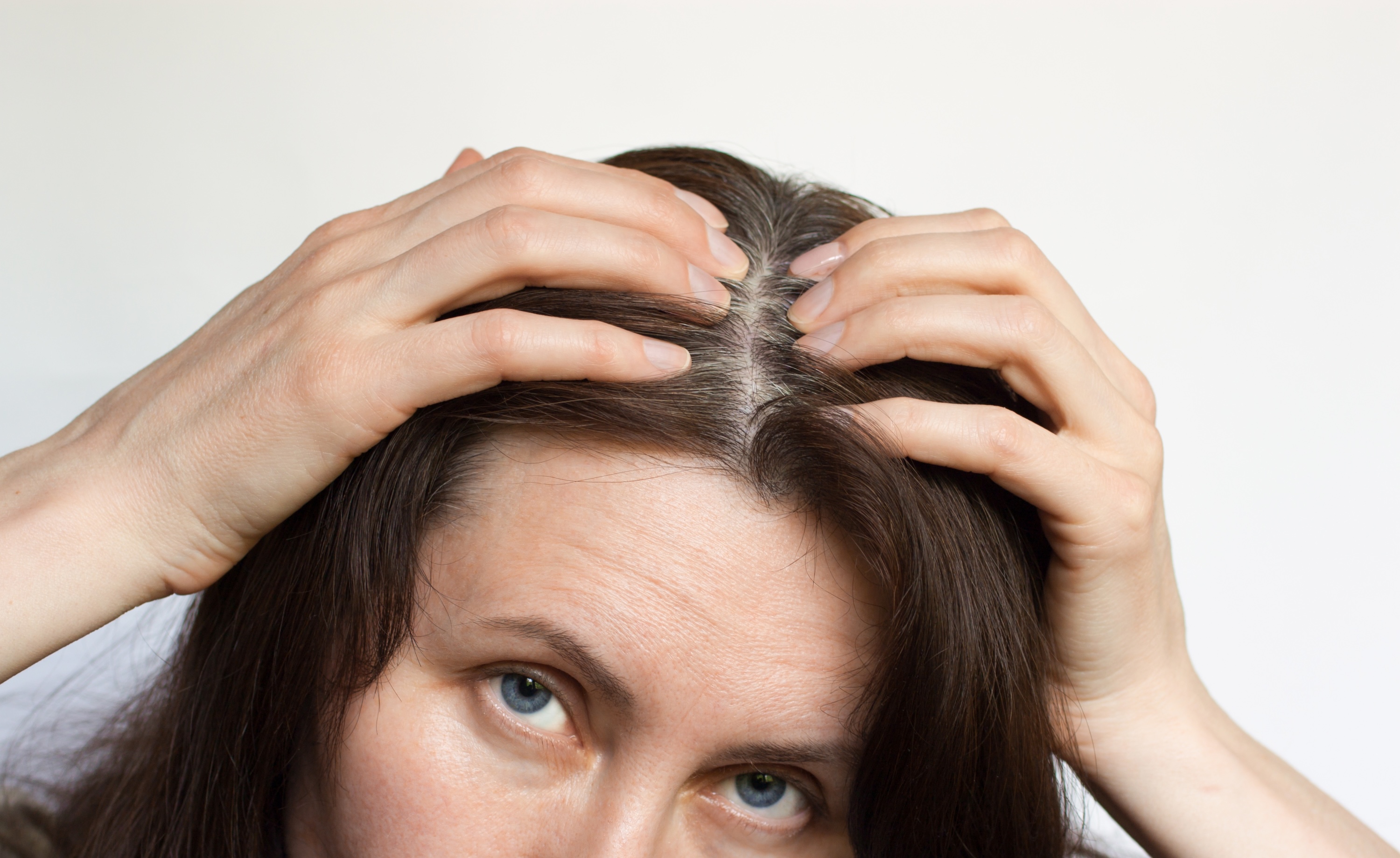 Woman examining hair in mirror showing hair thinning concerns